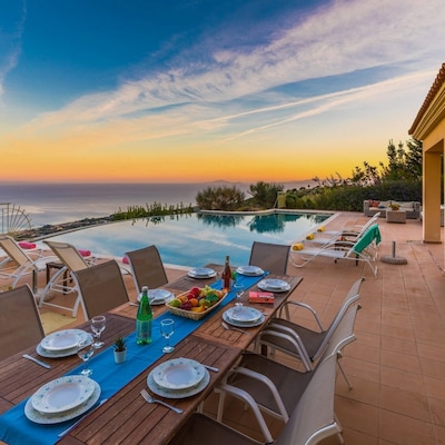 A private infinity pool at sunset, surrounded by sun loungers and a dining table with place settings and a bowl of fruit.